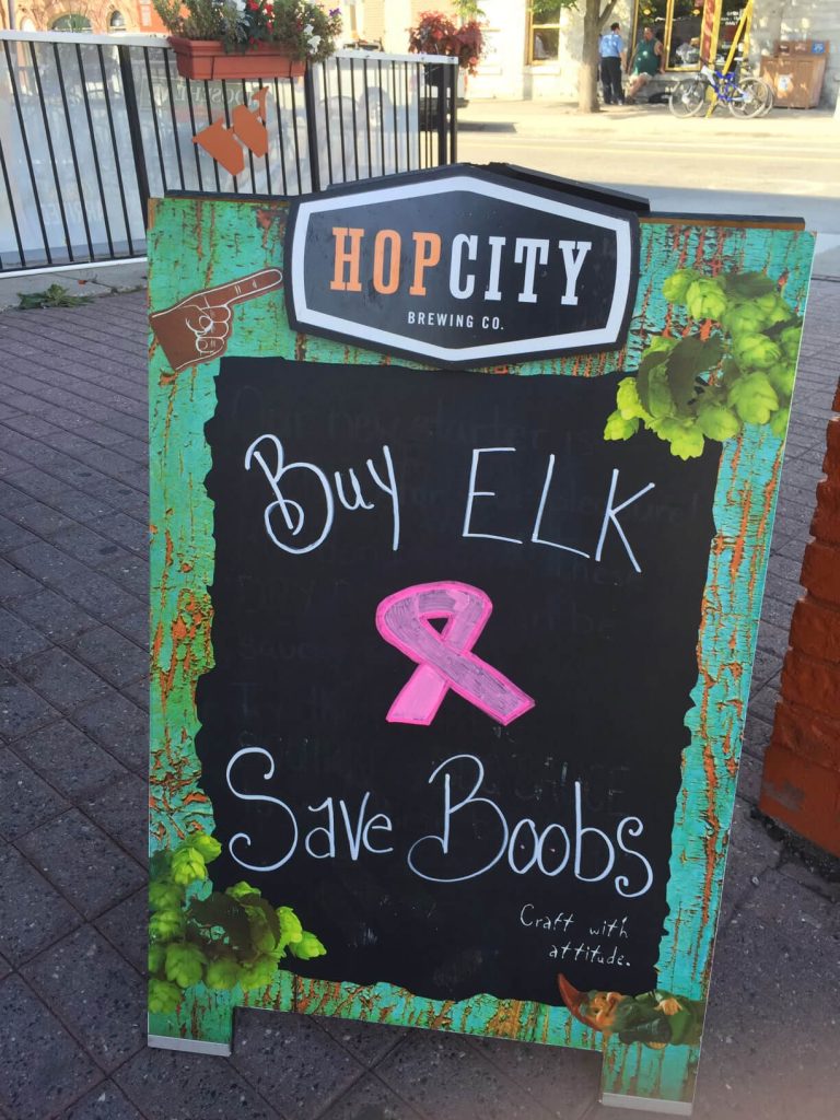 A sidewalk board sign that reads "buy elk, save boobs."