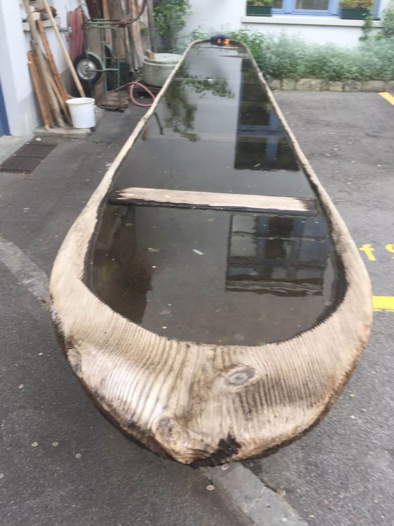 A rustic carved wooden canoe sits outside and is full to the brim with water.