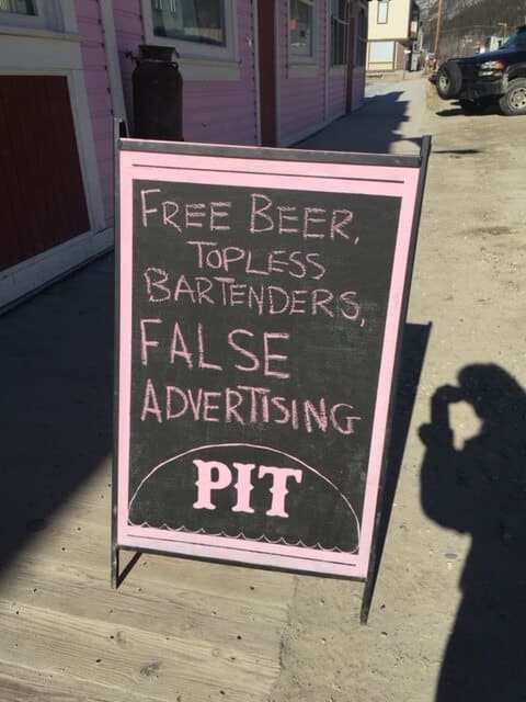 Sidewalk board sign that reads "free beer, topless bartenders, false advertising".