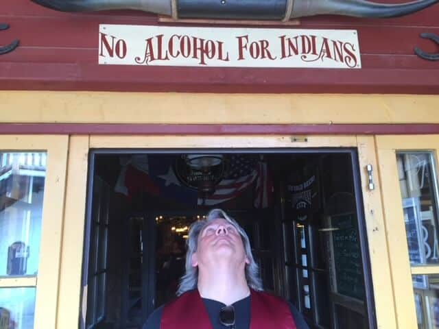 Drew is standing under a sign above a door that reads "no alcohol for Indians"