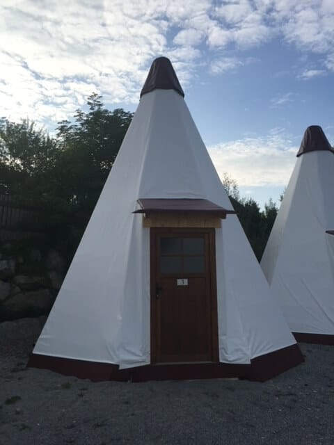 Photo of a small teepee shaped building with a traditional front door