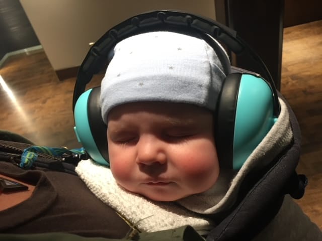 A sleeping baby wears hearing protection earmuffs